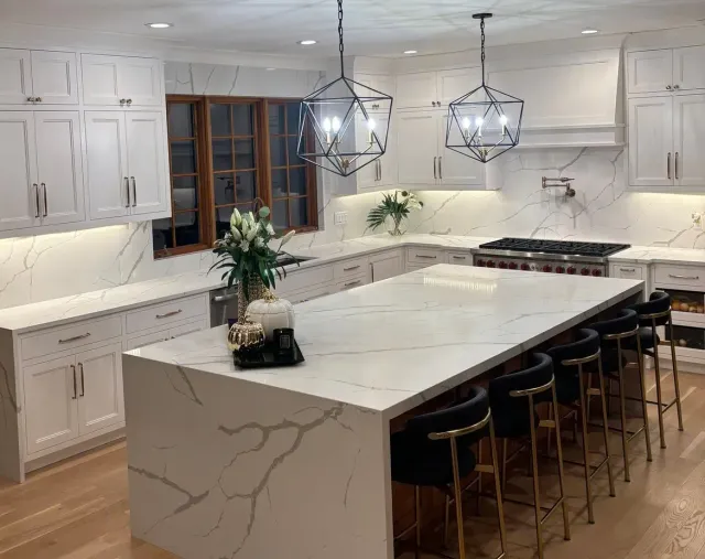 Bright modern kitchen with white cabinets, marble island, pendant lights, and bar stools