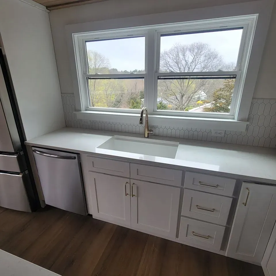A kitchen with white cabinets , a sink , a refrigerator and a window.