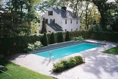 Private backyard with a rectangular swimming pool surrounded by a paved patio, green grass, and lush trees.