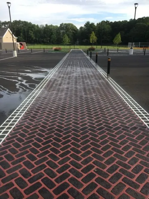 A brick walkway in a parking lot with trees in the background