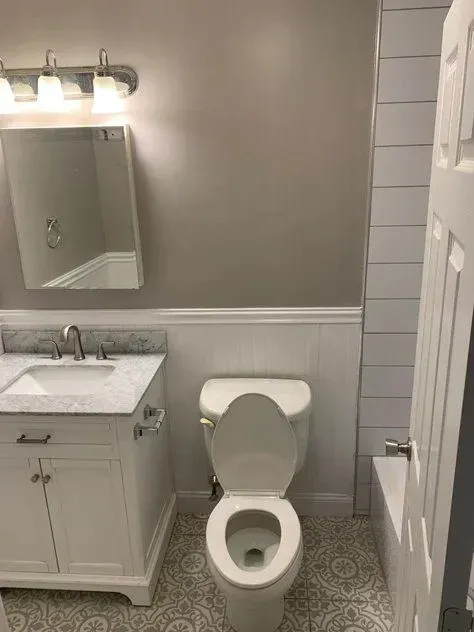 A bathroom with a toilet, sink, mirror and bathtub.