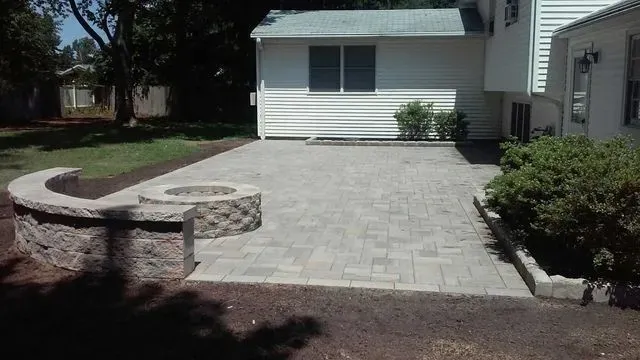 Paved front patio with a curved stone bench beside a white house