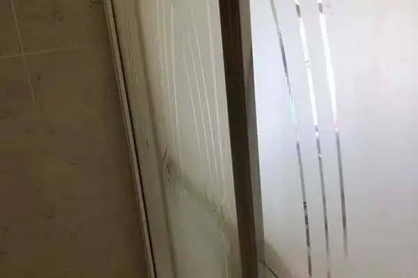 Frosted glass shower door with vertical striped design next to a tiled wall.