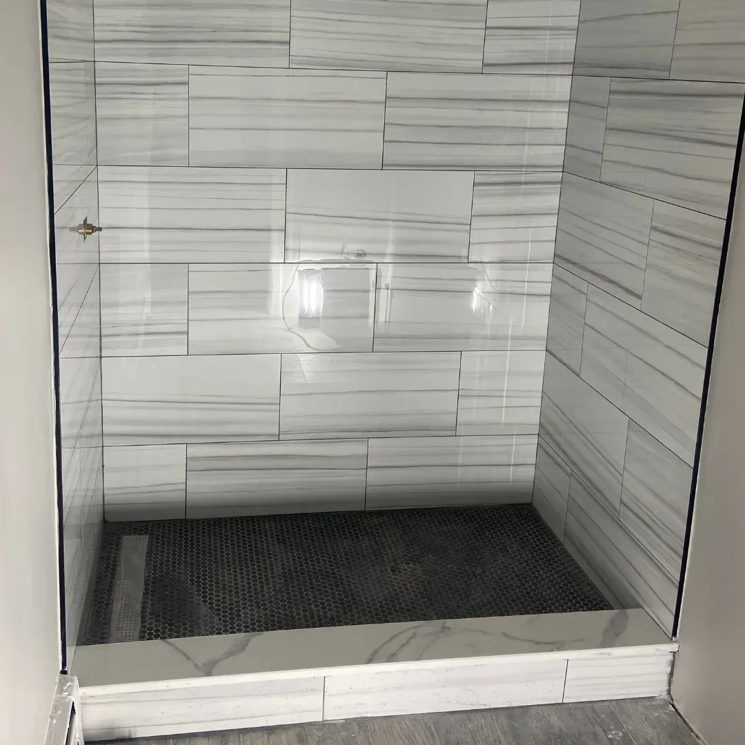 Walk-in shower remodel with white marble walls and black hex penny tile floor by SF Construction in Worcester, MA