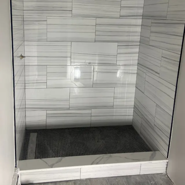 Walk-in shower remodel with white marble walls and black hex penny tile floor by SF Construction in Worcester, MA