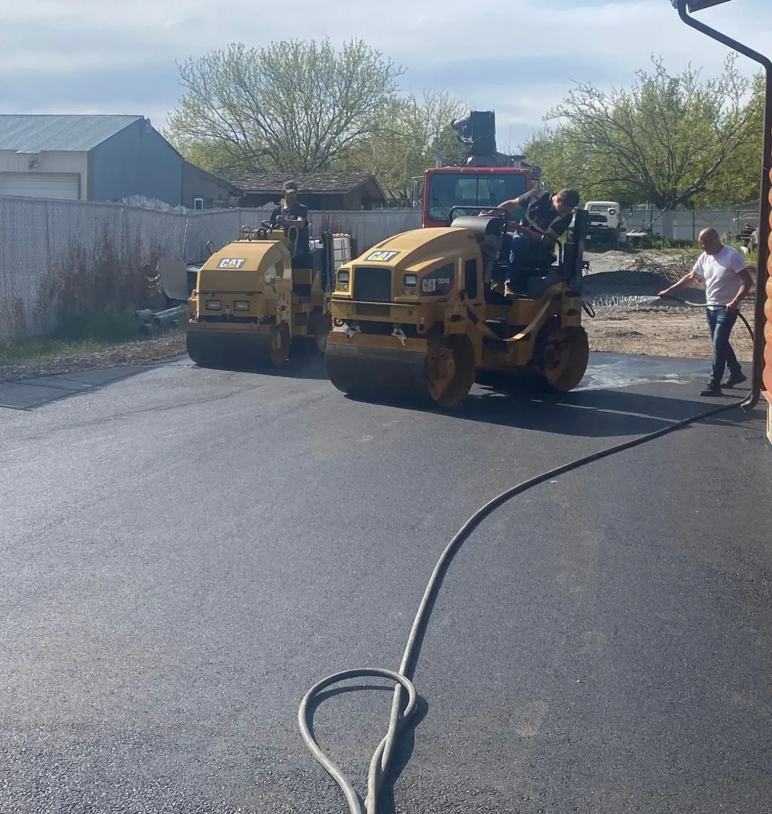 Two yellow road rollers compacting asphalt; a worker hoses down the surface.