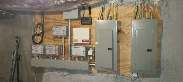Basement wall with electrical panels, meters, and exposed wiring in a utility area