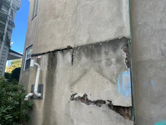 The side of a building with a hole in it and a pipe coming out of it