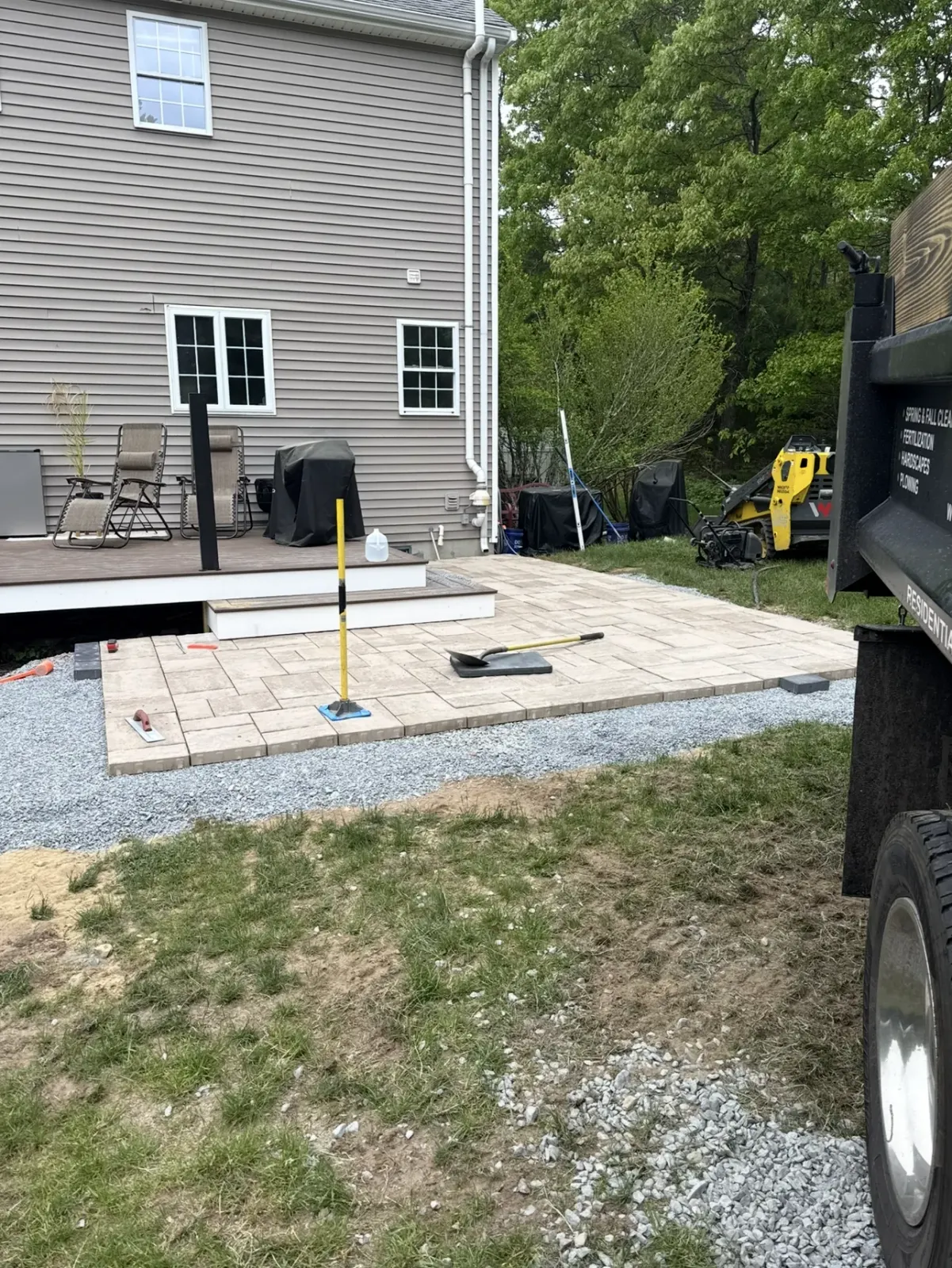 Backyard patio under construction with pavers, gravel, and a partially visible house.