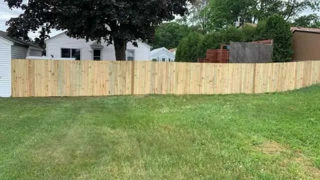 New wooden privacy fence across a grassy backyard with houses and trees behind it