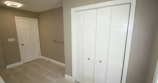 Empty beige bedroom with white closet doors, a white entry door, and tiled floor.