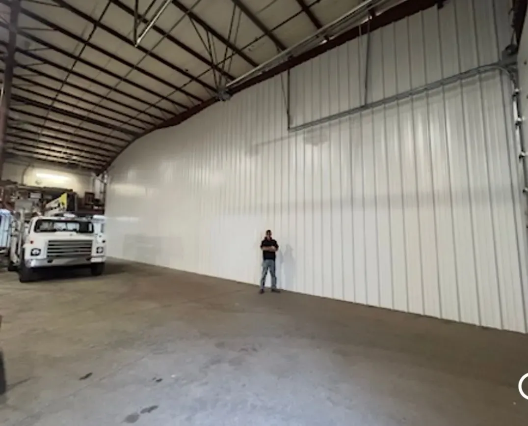 Large warehouse interior with a white wall, a parked truck, and a person standing near the wall