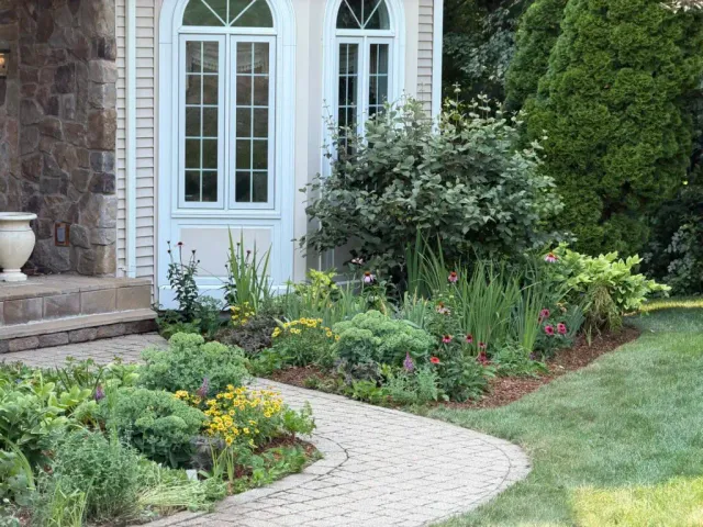 Perennial foundation garden with flowering plants and a curved walkway beside a home