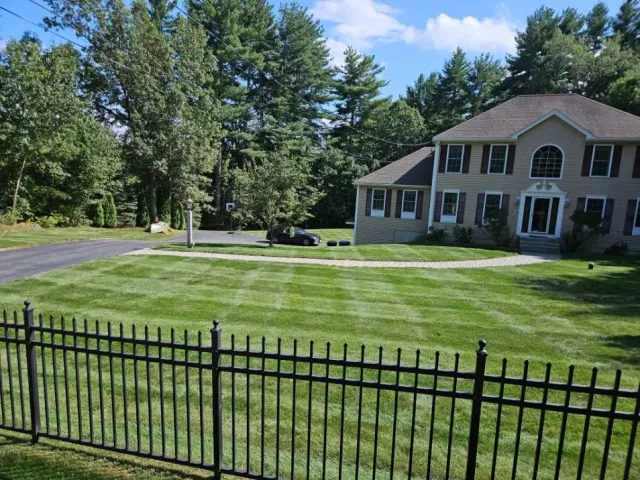 Freshly mowed front lawn with stripes behind a black iron fence in Hudson, NH