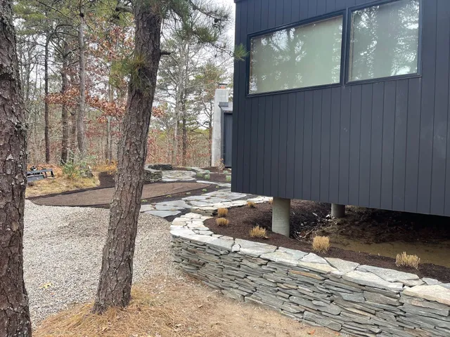A black house is surrounded by trees and a stone wall.