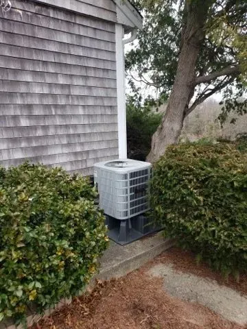 An air conditioner is sitting on the side of a house next to a tree.