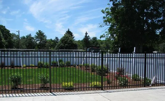 Black metal fence surrounds a small grassy area with landscaping under a blue sky.