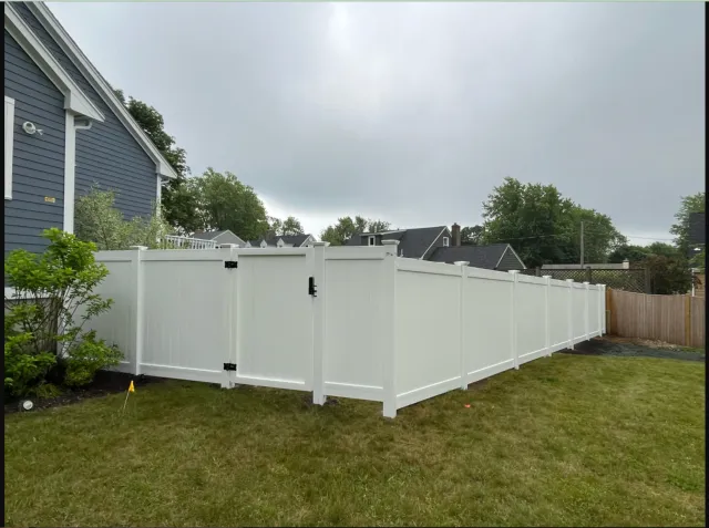 A white fence is in the backyard of a house.
