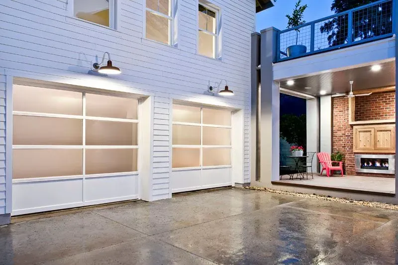 Two-car garage with frosted glass doors, next to an open patio with red chair, at dusk.