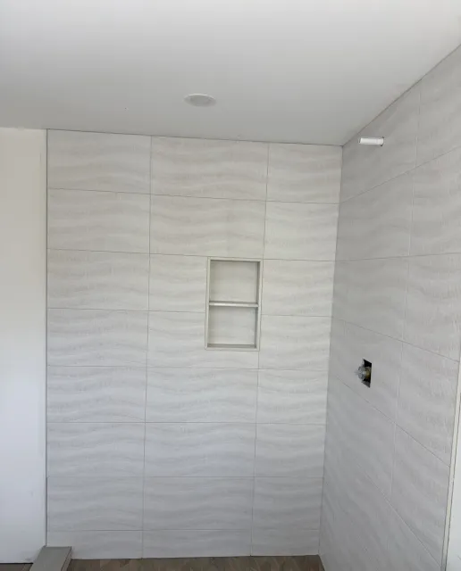 Shower clad in large-format textured wall tile with a two-shelf niche