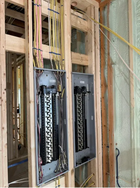 Electrical wiring and circuit breaker panels installed in a wooden framing wall under construction.