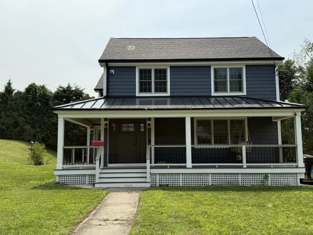 Newly built home with gray siding, a standing seam roof and a covered front porch