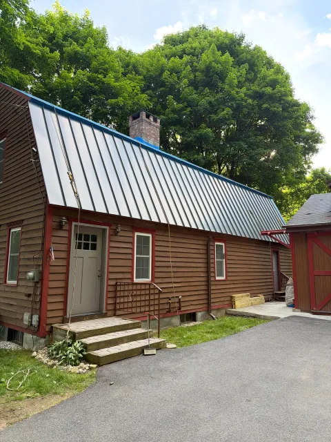 Rustic red barn-style building with metal roof, steps, gravel path, and trees in the background