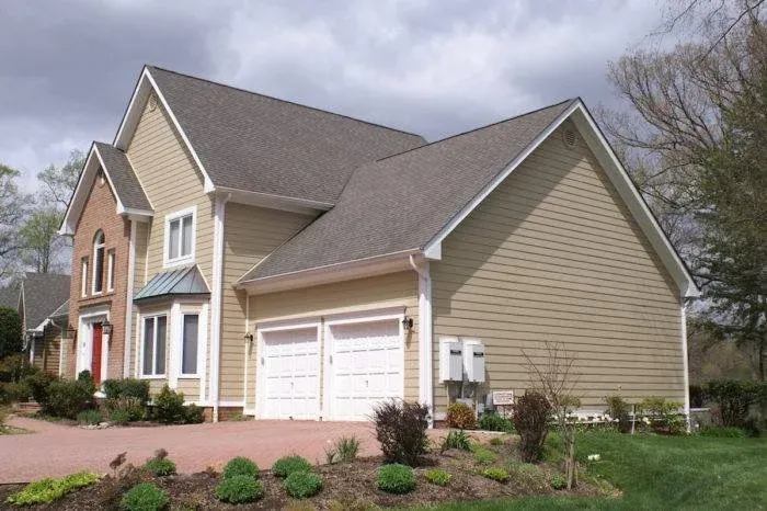 Front view of a two-story house with beige siding, a two-car garage, and a well-maintained front yard with small shrubs and plants.