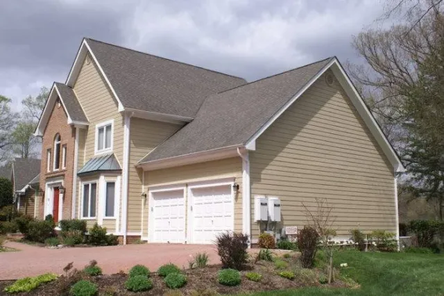 Front view of a two-story house with beige siding, a two-car garage, and a well-maintained front yard with small shrubs and plants.