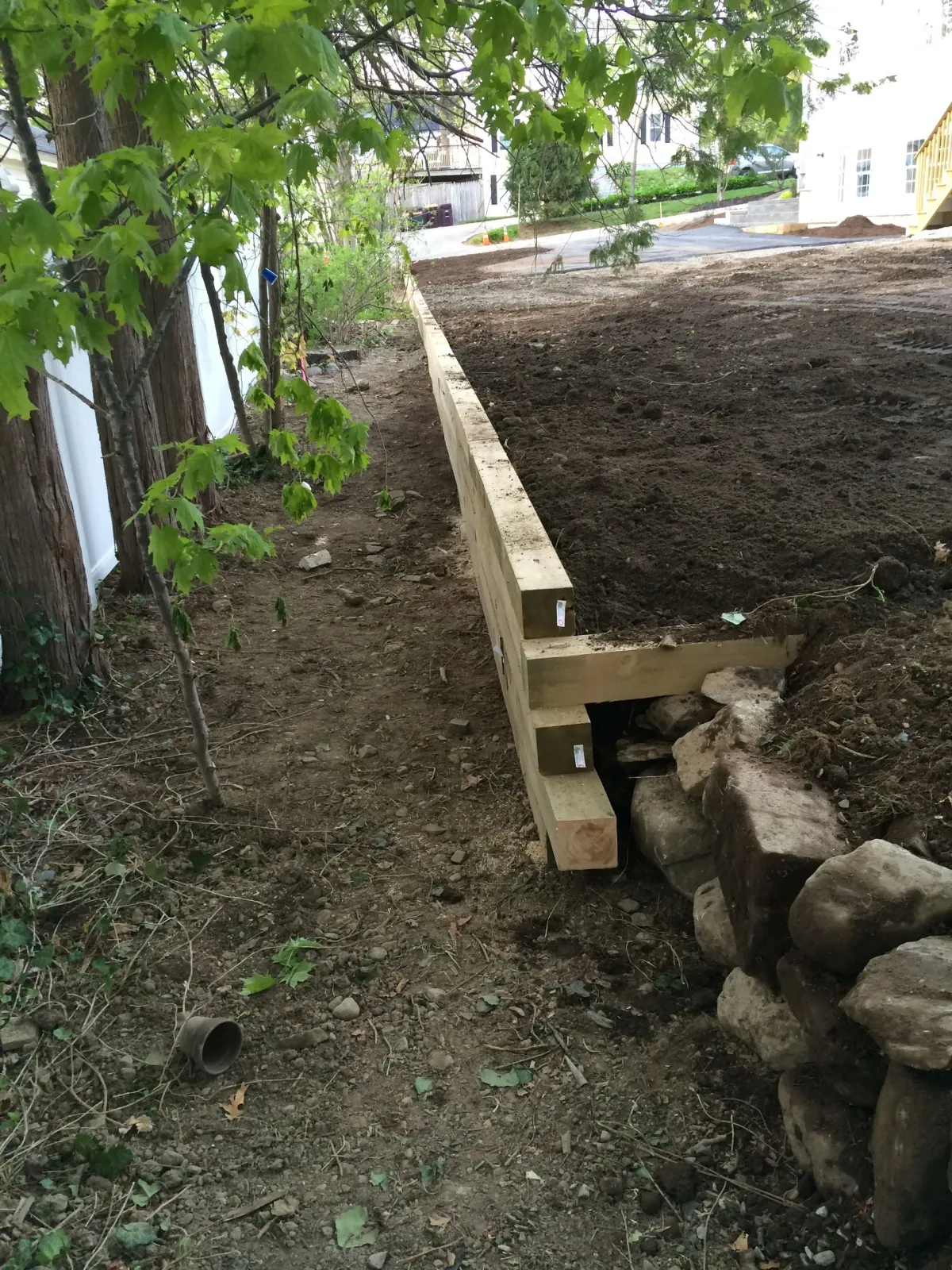 Wooden retaining wall with rocks, soil, and trees.