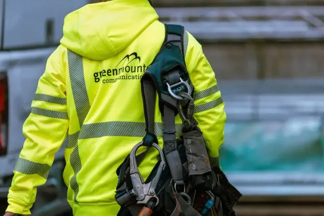 Worker wearing a neon yellow safety jacket with reflective stripes holds climbing gear and harness.