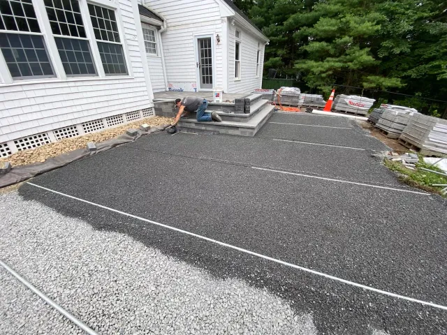 Paver patio base preparation with compacted stone, screed rails, and foundation drainage during installation, Southeastern MA