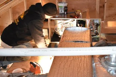 HVAC technician inspecting ductwork and system components in Cape Cod attic.