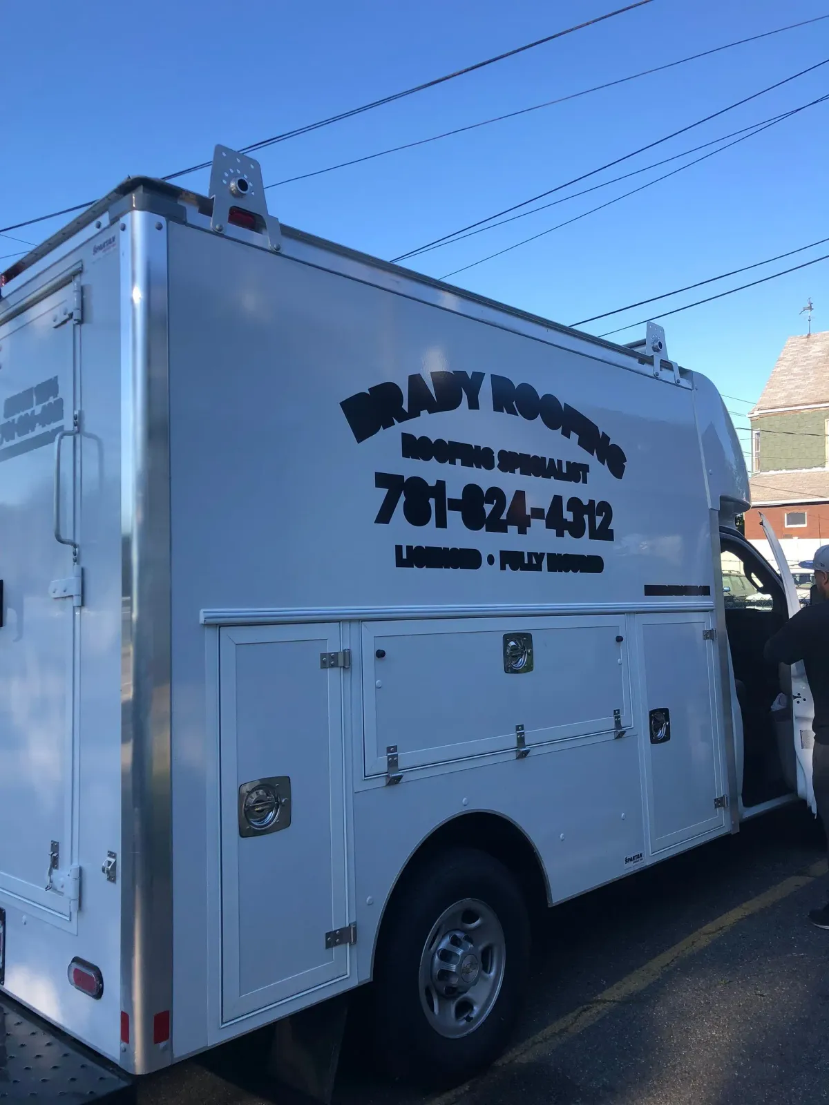 White utility truck with side compartments and black company lettering parked on a street.