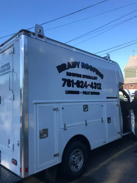 White utility truck with side compartments and black company lettering parked on a street.