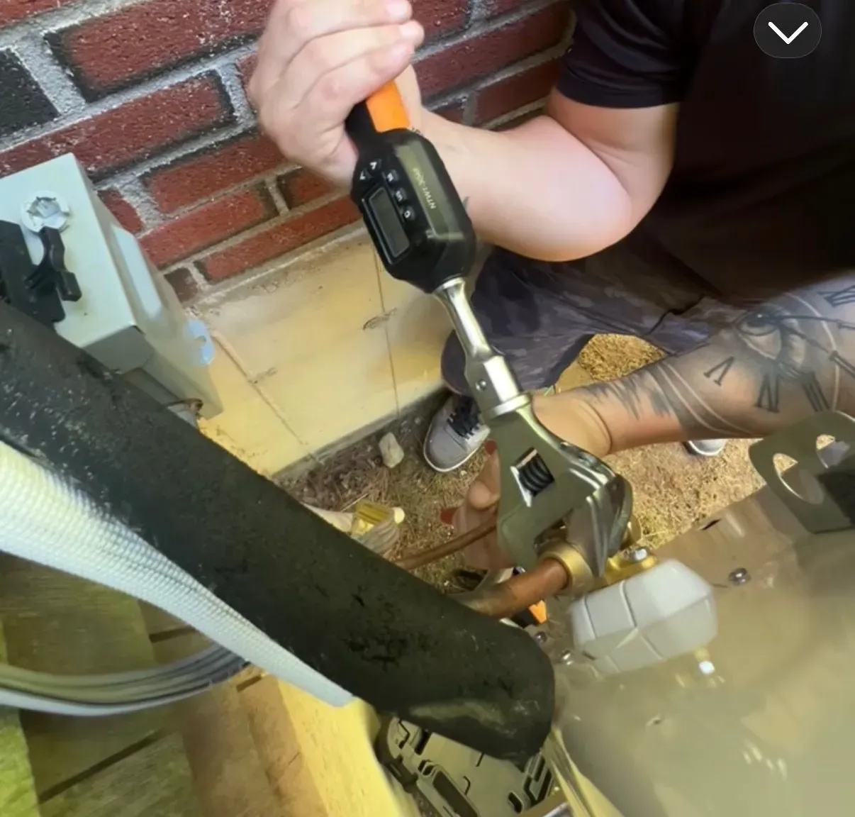 Person tightening a bolt with a ratchet near a brick wall and outdoor utility equipment