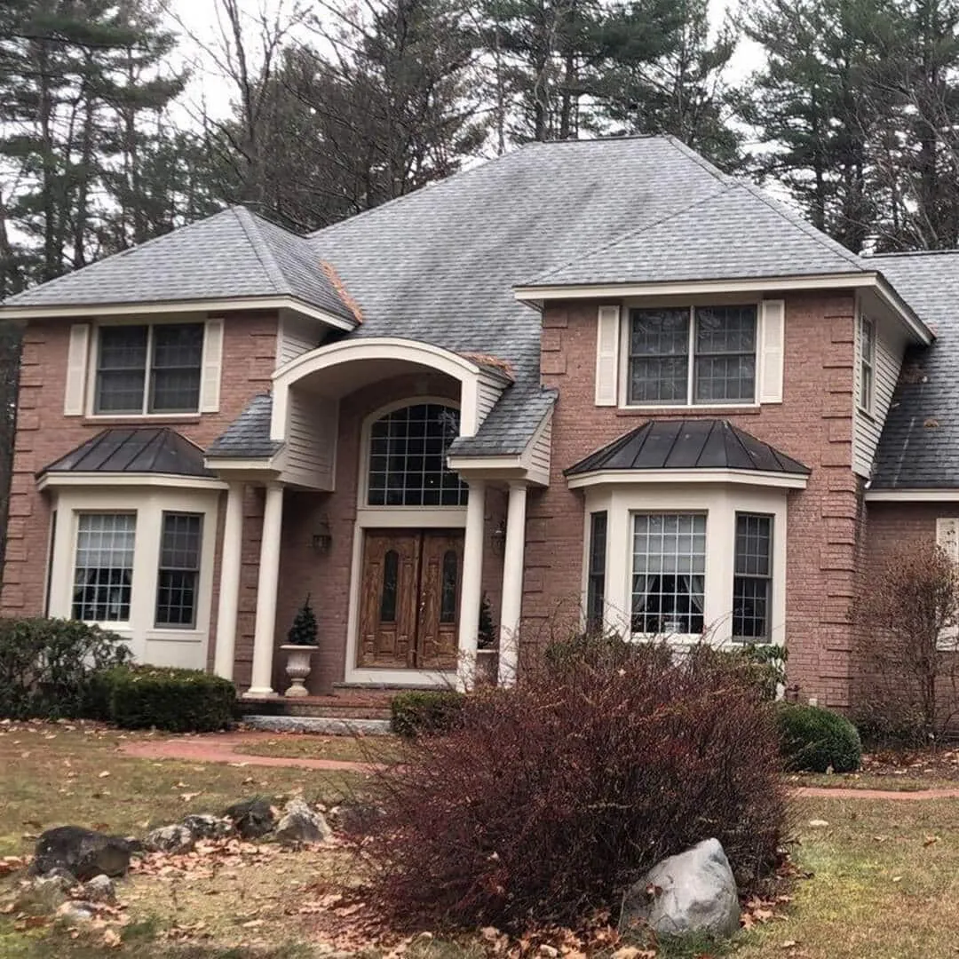 Two-story-brick-house-with-gray-roof,-large-windows,-and-landscaped-entrance