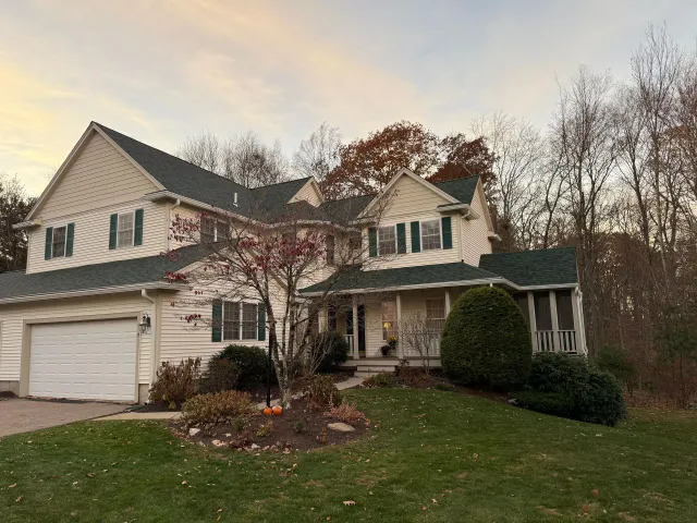 Two-story beige suburban house with a garage, front porch, and leafless trees at dusk