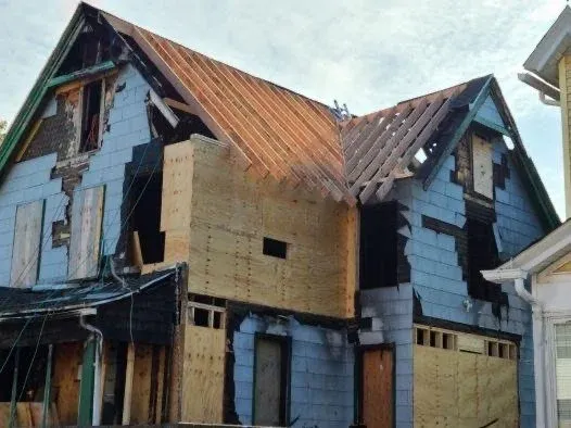 House under renovation with exposed blue siding and plywood, partially covered with a rusted metal roof.