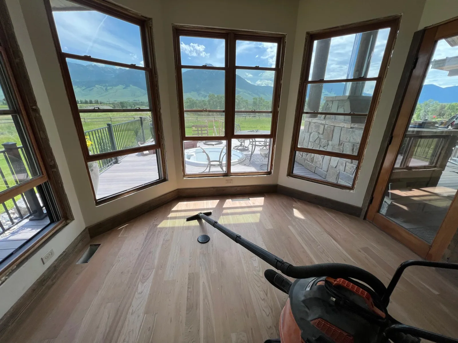 Empty room with large windows showing scenic mountain landscape, hardwood floor, and a vacuum cleaner on the floor.