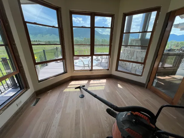 Empty room with large windows showing scenic mountain landscape, hardwood floor, and a vacuum cleaner on the floor.