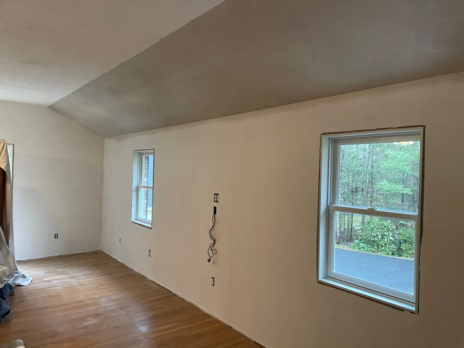 Empty room with white walls, two windows, hardwood floor, and unfinished electrical outlets.