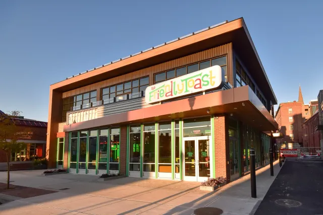 Building with a colorful sign that reads 'the Friedly Toast' and large windows, located in an urban area during sunset.