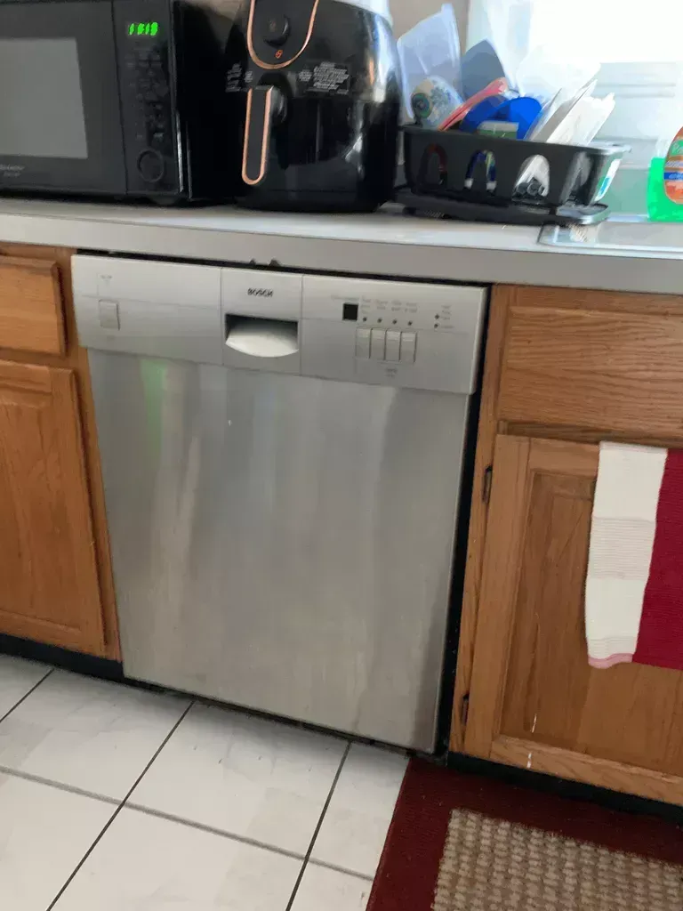 Kitchen with a stainless steel dishwasher between wood cabinets under a countertop with appliances.