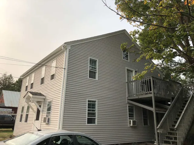A three-story, light gray siding building with a wooden exterior staircase leading to a second-floor deck.