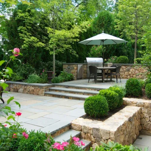 A Wellesley stone patio and terrace design uses masonry steps, layered grade changes, and elegant planting to connect the home and garden.