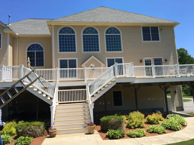 Rear view of a beige two-story house with a large deck and outdoor staircase