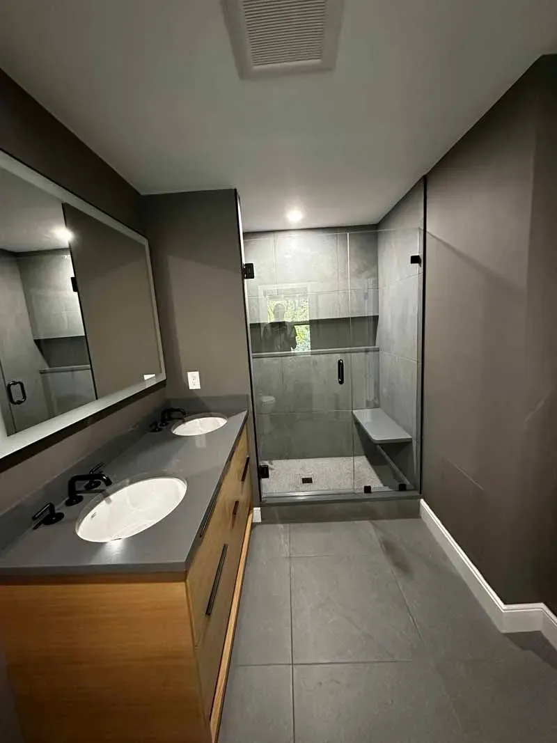 Modern bathroom with double vanity, gray tile, and glass shower.