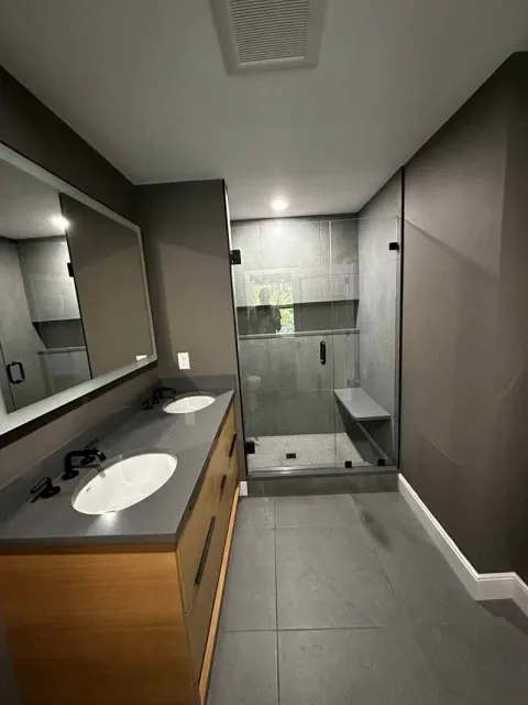 Modern bathroom with double vanity, gray tile, and glass shower.