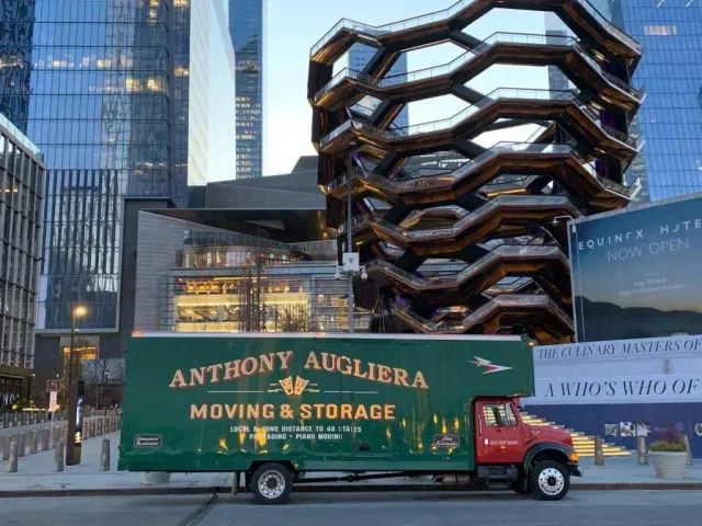 A green moving truck is parked on the side of the road in front of a building.